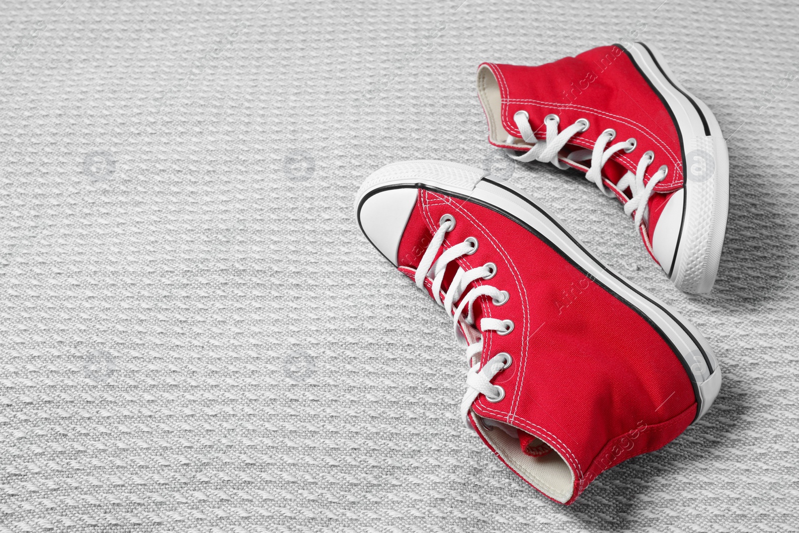 Photo of Pair of new stylish red sneakers on light grey fabric. Space for text