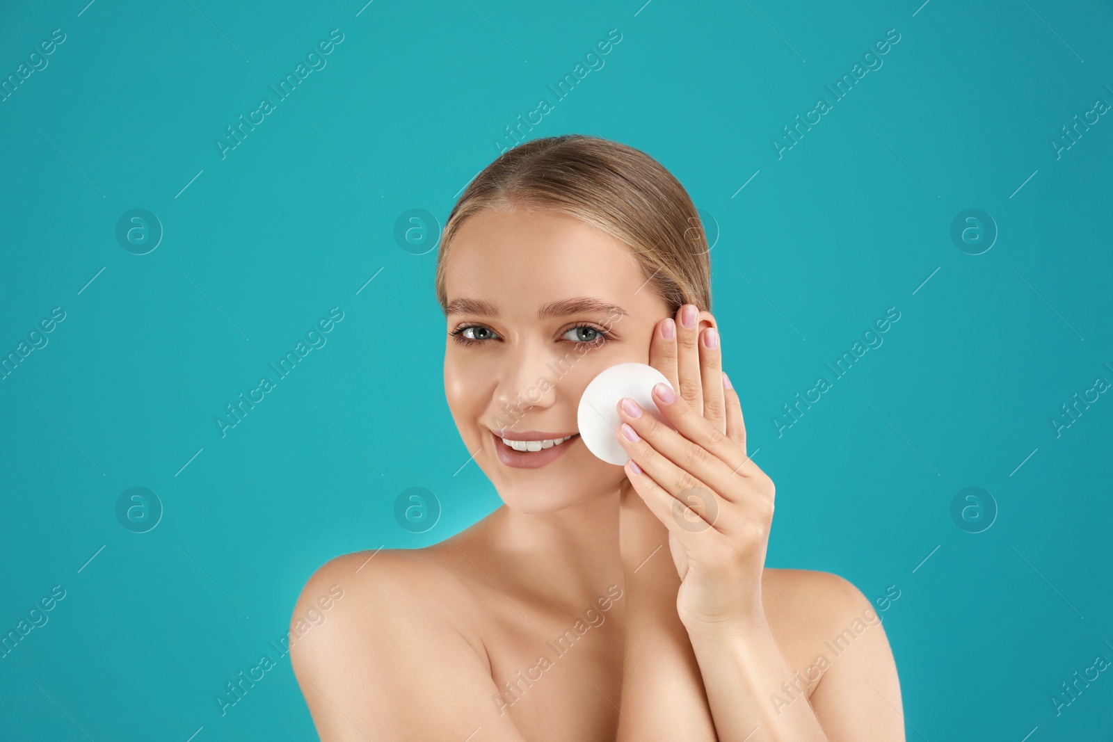 Photo of Beautiful young woman with cotton pad on turquoise background