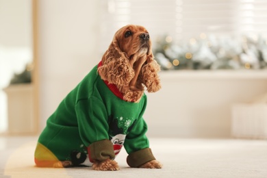 Adorable Cocker Spaniel in Christmas sweater on blurred background, space for text