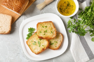 Photo of Slices of toasted bread with garlic and herb on light grey marble table, flat lay