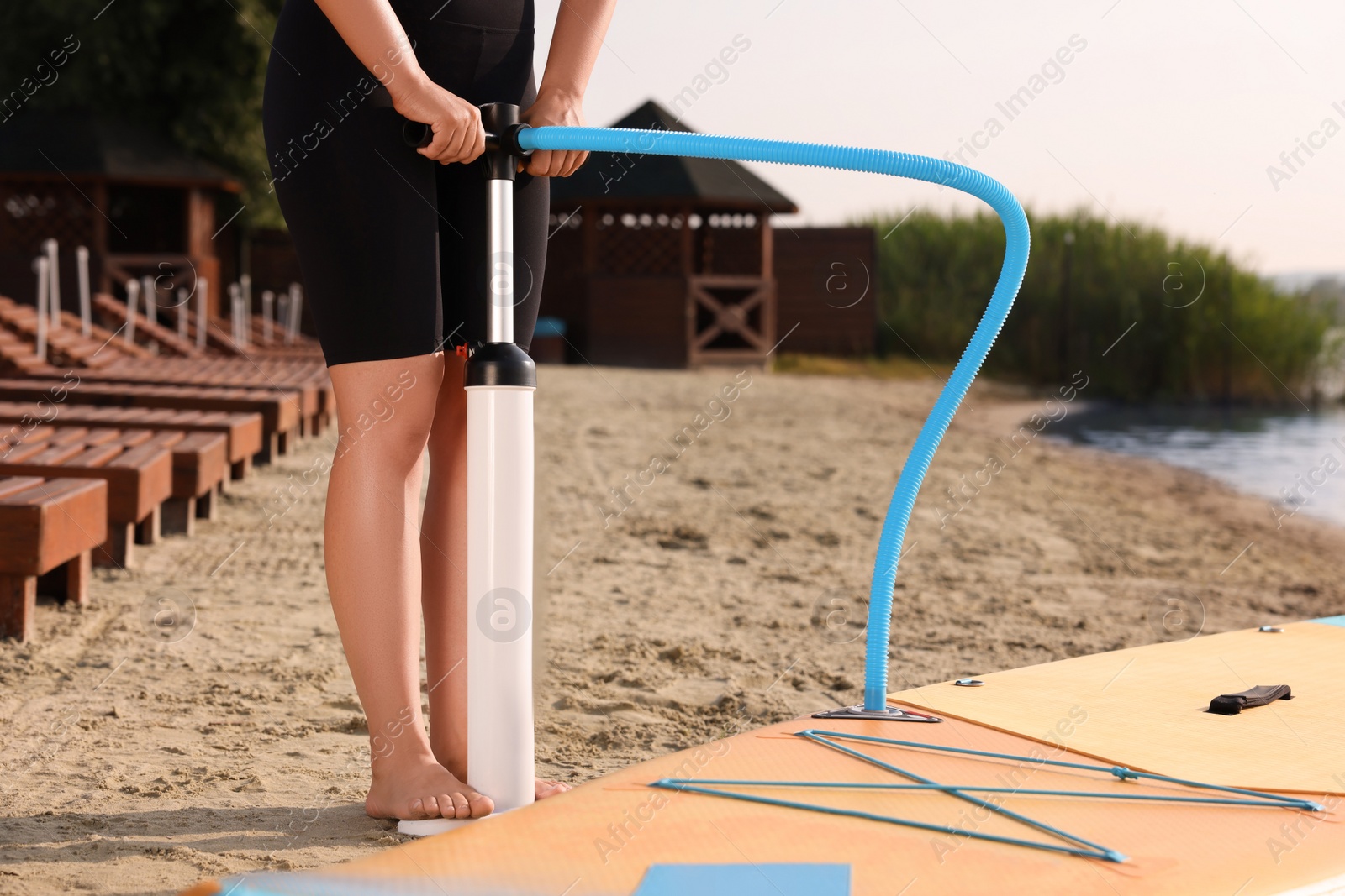 Photo of Woman pumping up SUP board on river shore, closeup