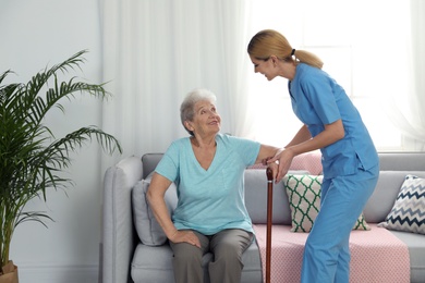 Photo of Nurse assisting elderly woman with cane indoors