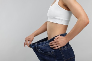 Slim woman wearing big jeans on grey background, closeup. Weight loss