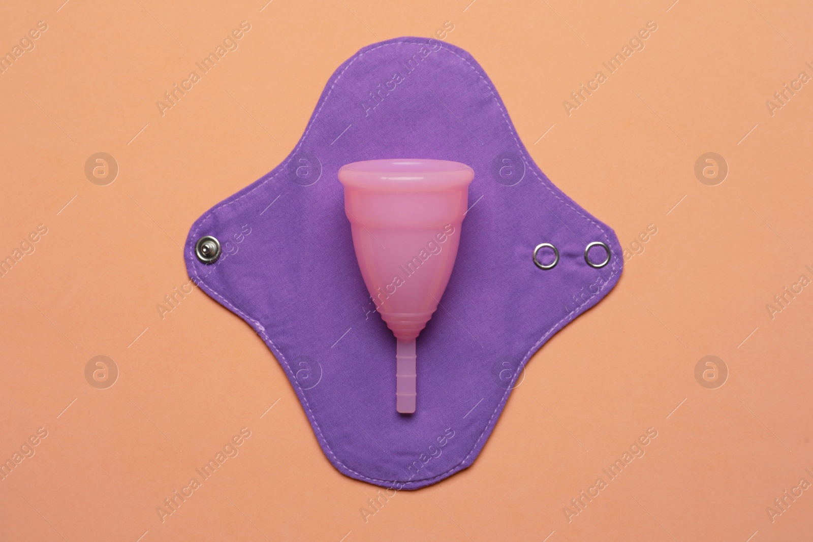 Photo of Menstrual cup and cloth pad on pale orange background, top view. Reusable feminine hygiene products