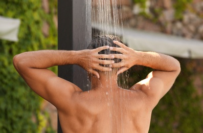 Photo of Man washing hair in outdoor shower on summer day