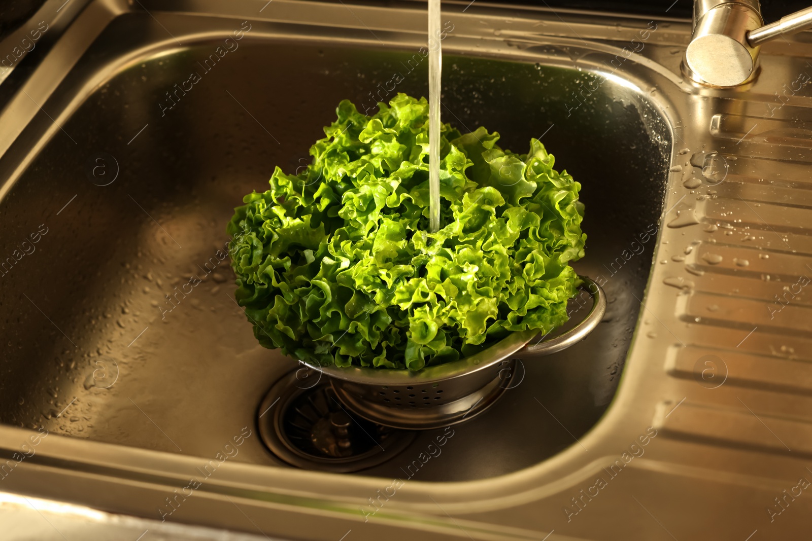 Photo of Woman washing fresh lettuce leaves in metal colander, closeup