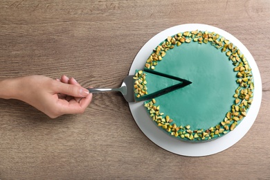 Woman with tasty spirulina cheesecake on wooden table, top view