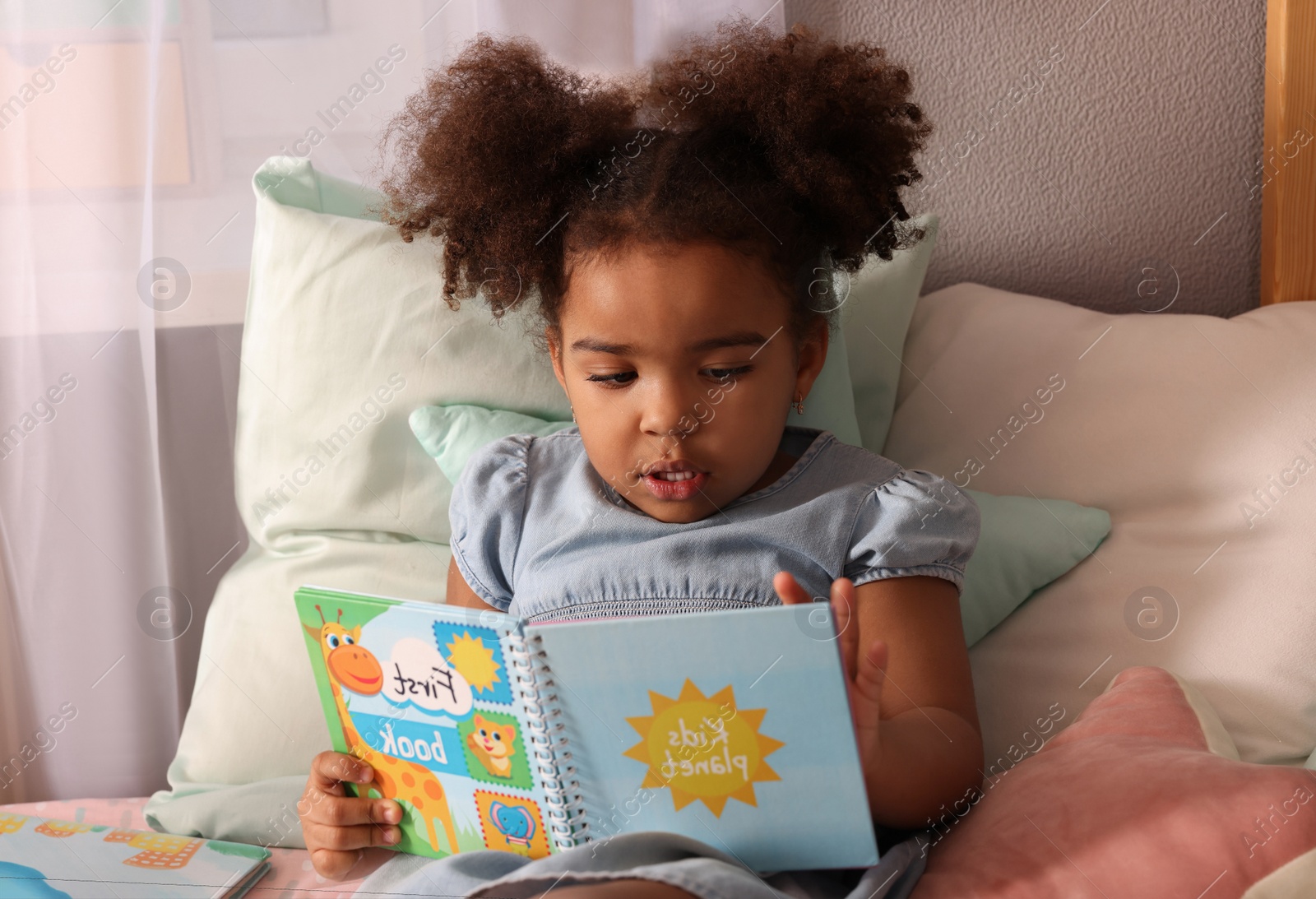 Photo of African American girl reading book on bed at home