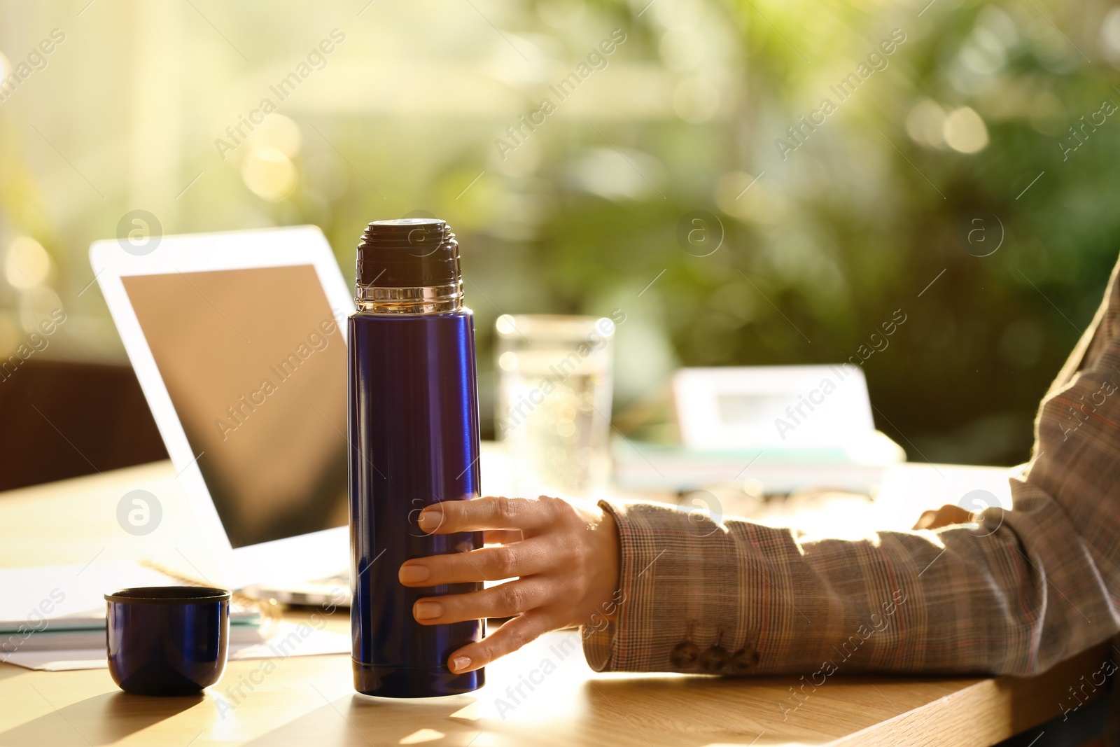 Photo of Woman with blue thermos bottle at workplace, closeup