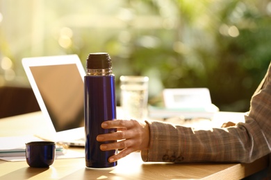 Woman with blue thermos bottle at workplace, closeup