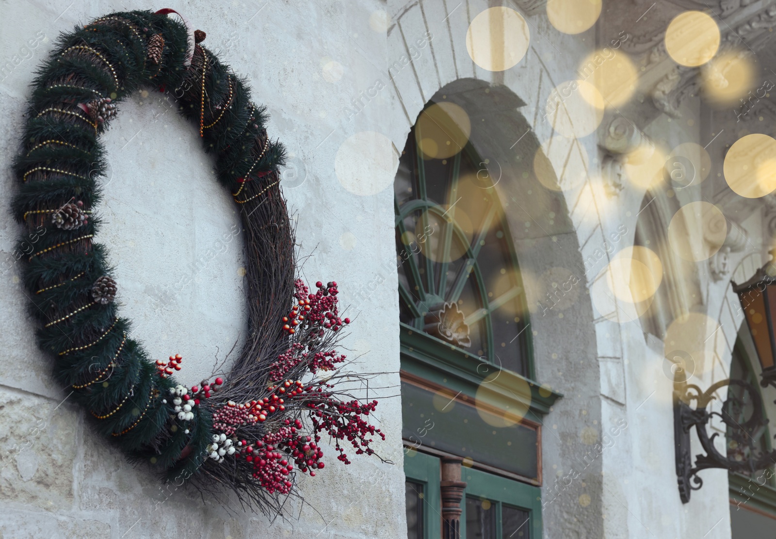 Photo of Beautiful Christmas wreath with berries and cones hanging on white wall outdoors