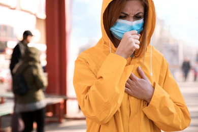 Photo of Woman with medical mask coughing on city street. Virus protection