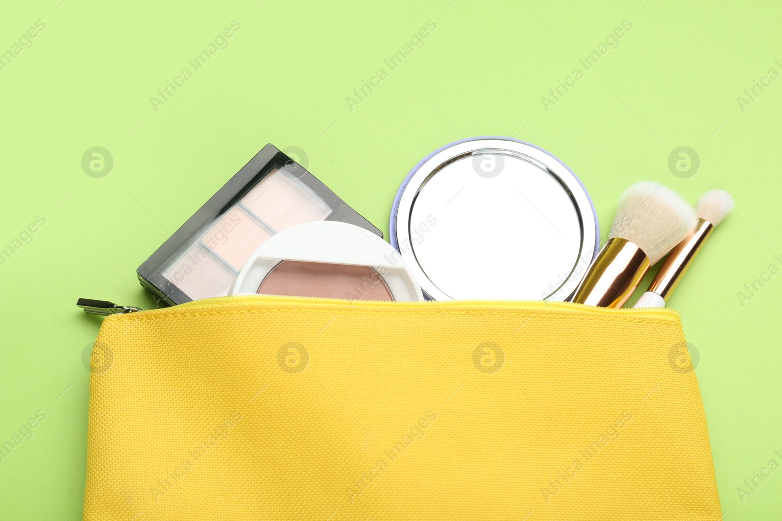 Photo of Cosmetic bag with pocket mirror and makeup products on light green background, flat lay