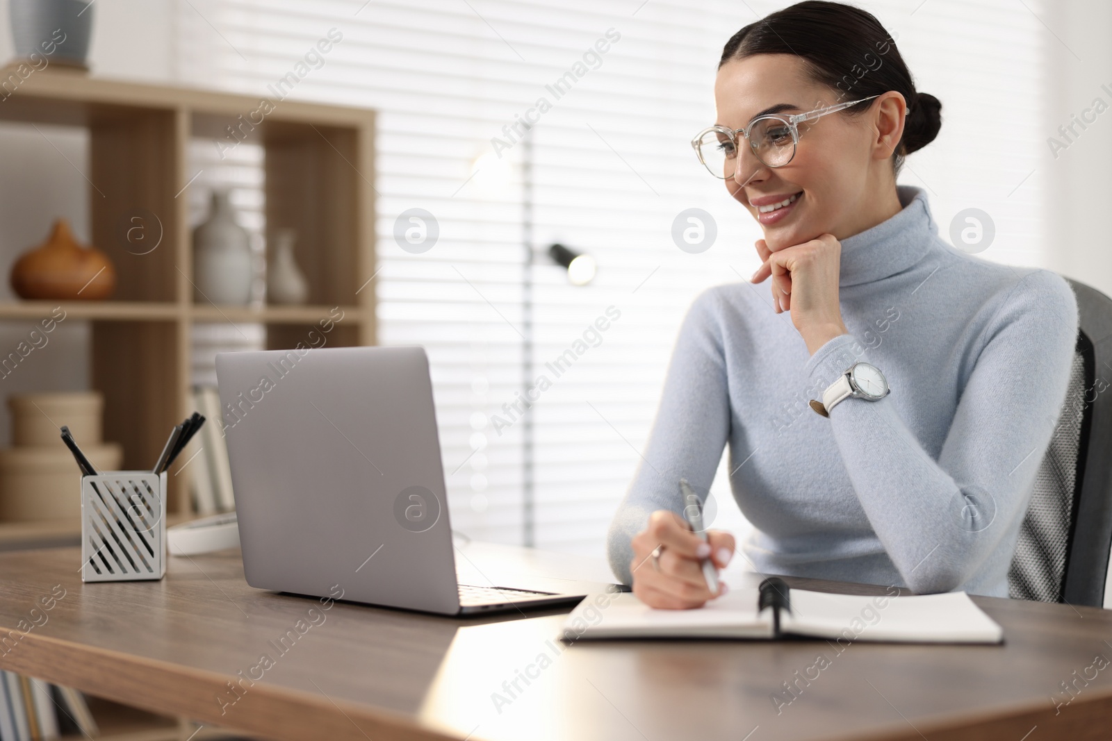 Photo of Young woman in glasses watching webinar at table in office