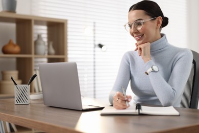 Young woman in glasses watching webinar at table in office