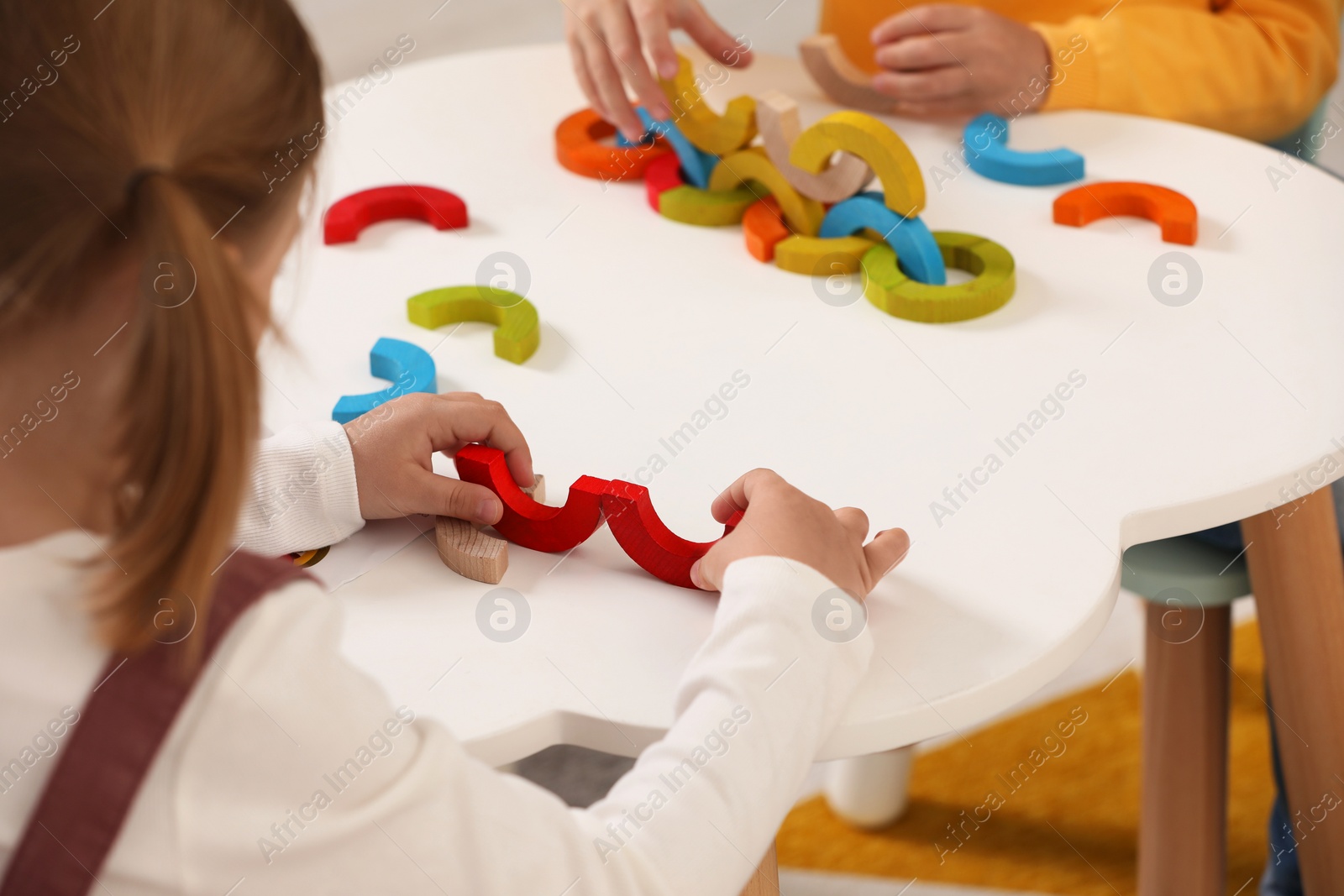 Photo of Little children playing with colorful wooden pieces at white table indoors, closeup. Developmental toy
