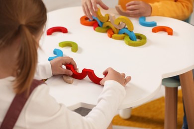 Photo of Little children playing with colorful wooden pieces at white table indoors, closeup. Developmental toy