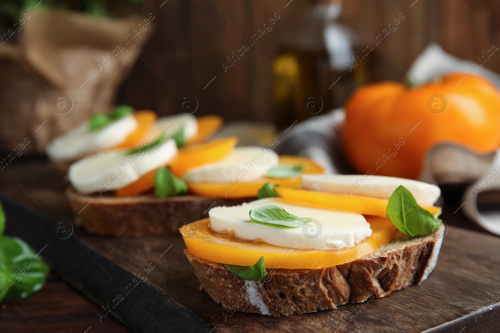 Photo of Delicious sandwiches with mozzarella, yellow tomatoes and basil on wooden board