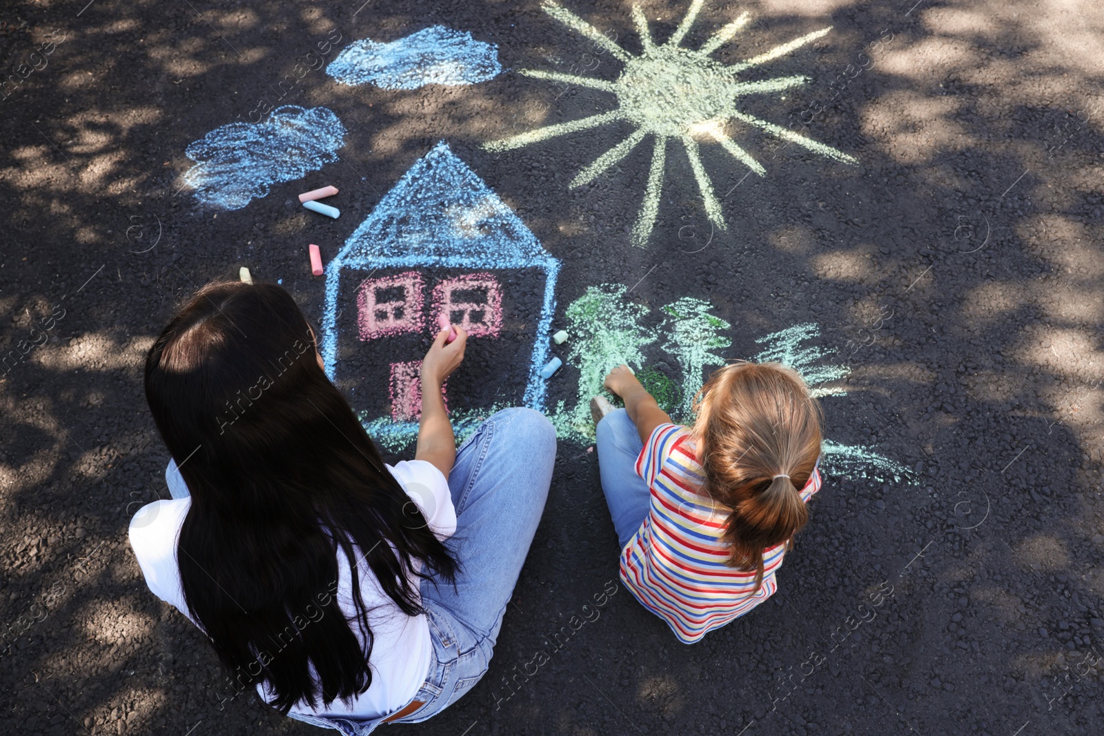 Photo of Little child and her mother drawing with colorful chalks on asphalt, above view