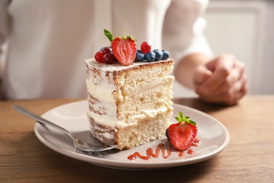 Photo of Piece of delicious homemade cake with fresh berries and blurred woman on background