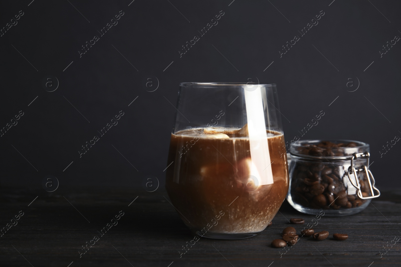 Photo of Coffee drink with milk ice cubes and beans on table against dark background. Space for text