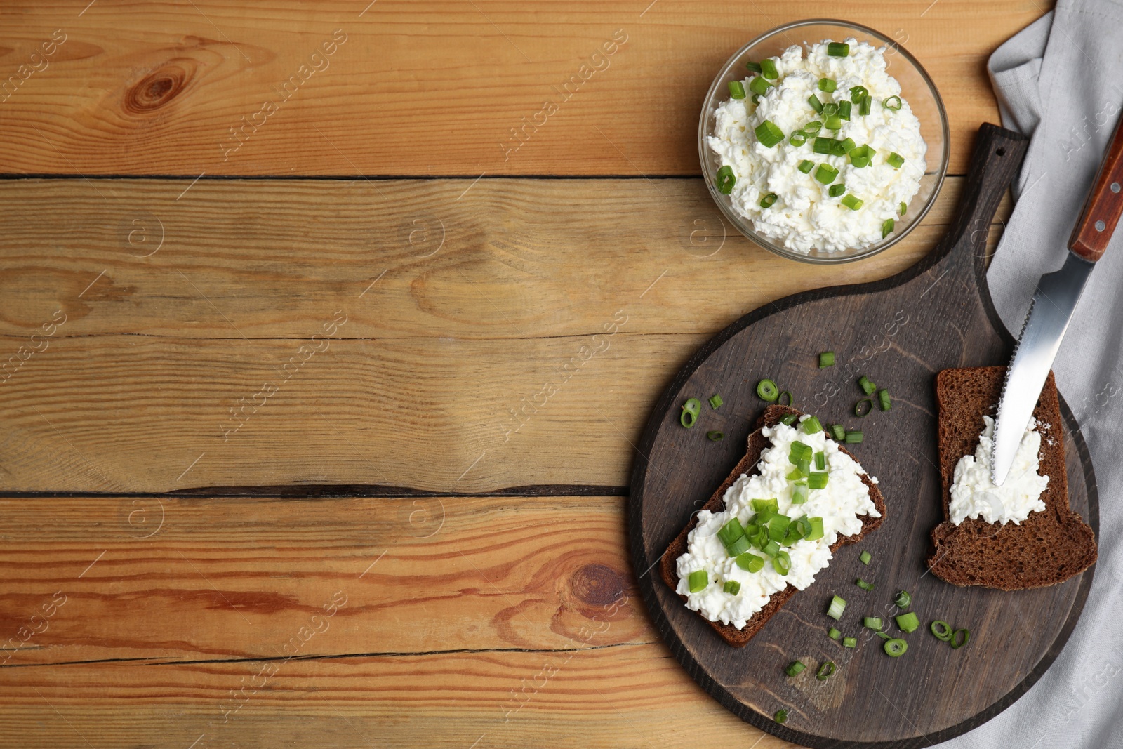 Photo of Bread with cottage cheese and green onion on wooden table, flat lay. Space for text