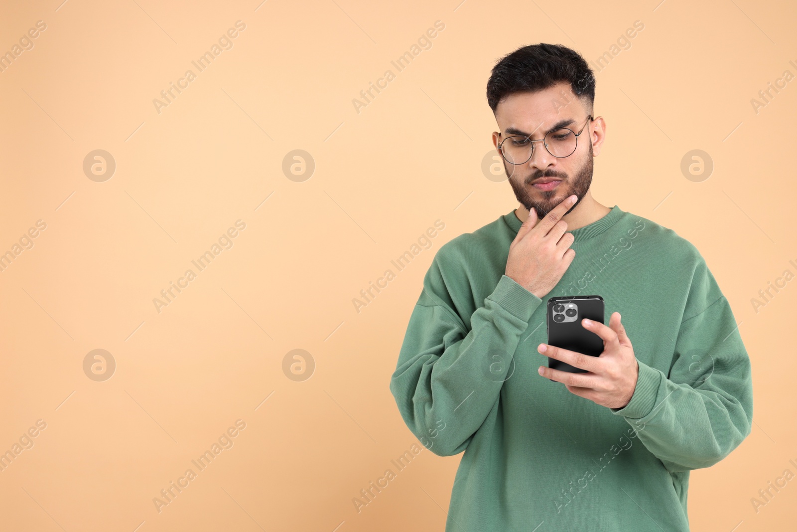 Photo of Handsome young man using smartphone on beige background, space for text
