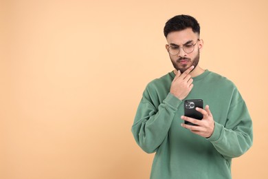 Handsome young man using smartphone on beige background, space for text