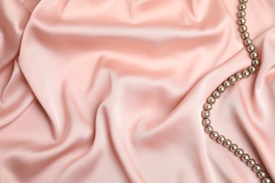 Photo of Beautiful pearls on pink silk, top view. Space for text