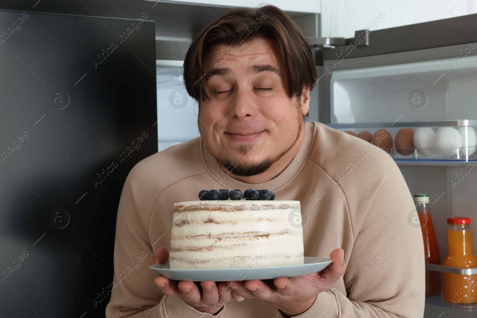 Photo of Happy overweight man with cake near open refrigerator in kitchen