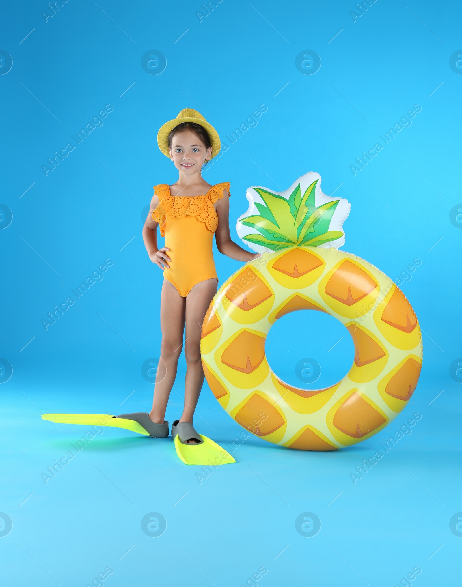 Photo of Cute little child in beachwear with inflatable ring on light blue background