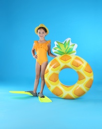 Cute little child in beachwear with inflatable ring on light blue background