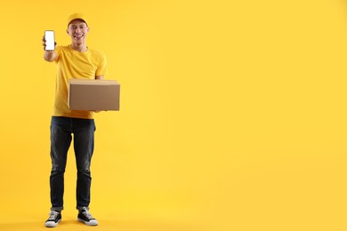 Happy courier with parcel and smartphone on orange background. Space for text