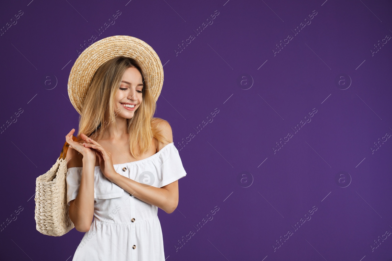 Photo of Beautiful young woman with stylish straw bag on purple background. Space for text