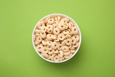 Photo of Tasty cereal rings in bowl on green table, top view