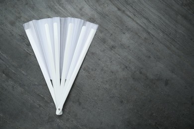 Stylish white hand fan on grey background, top view. Space for text