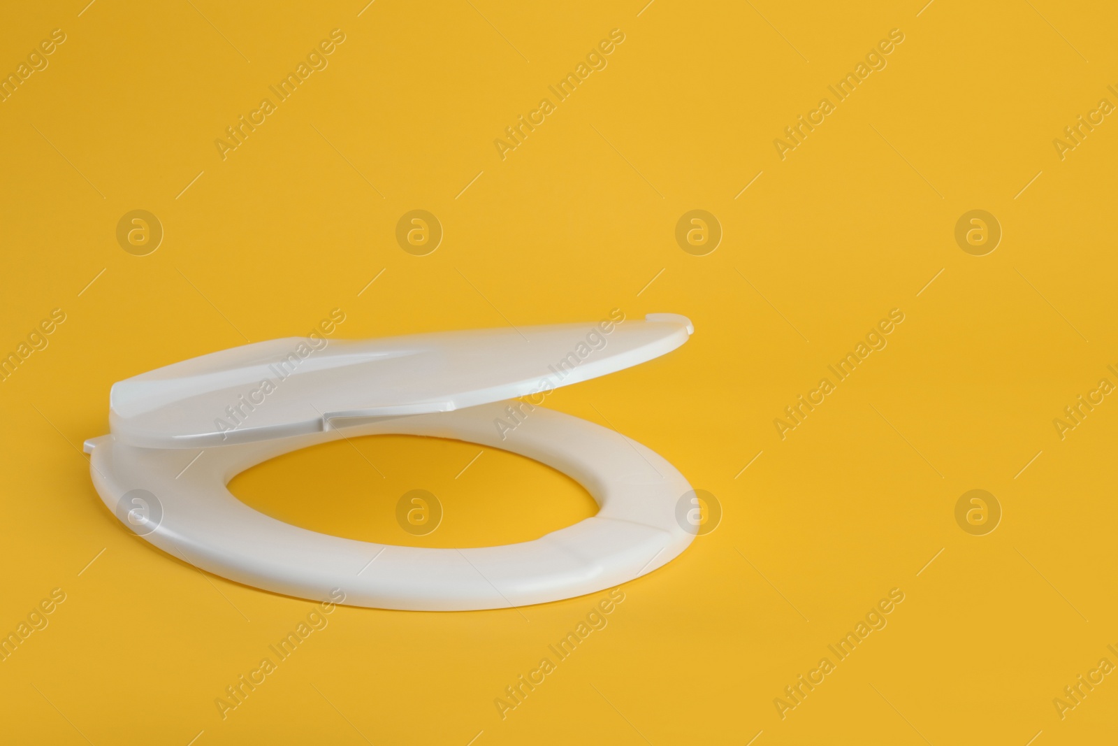 Photo of New white plastic toilet seat on yellow background, space for text