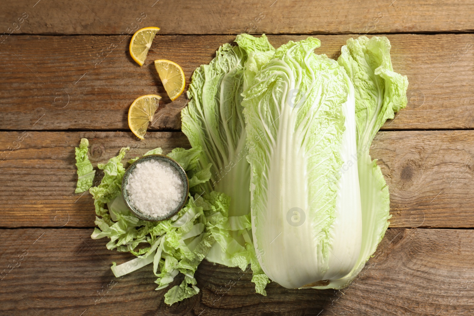 Photo of Fresh Chinese cabbage, salt and lemon on wooden table, flat lay