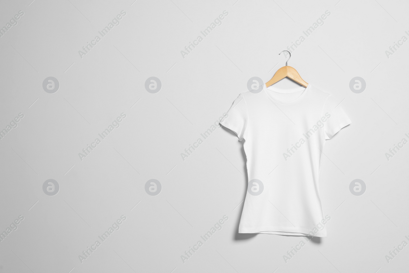 Photo of Hanger with white t-shirt on light wall. Mockup for design