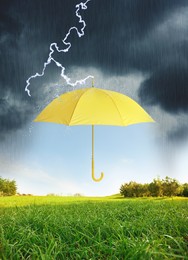 Image of Open yellow umbrella under heavy rain in green meadow