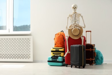 Photo of Waiting concept. Human skeleton with hat and suitcases indoors