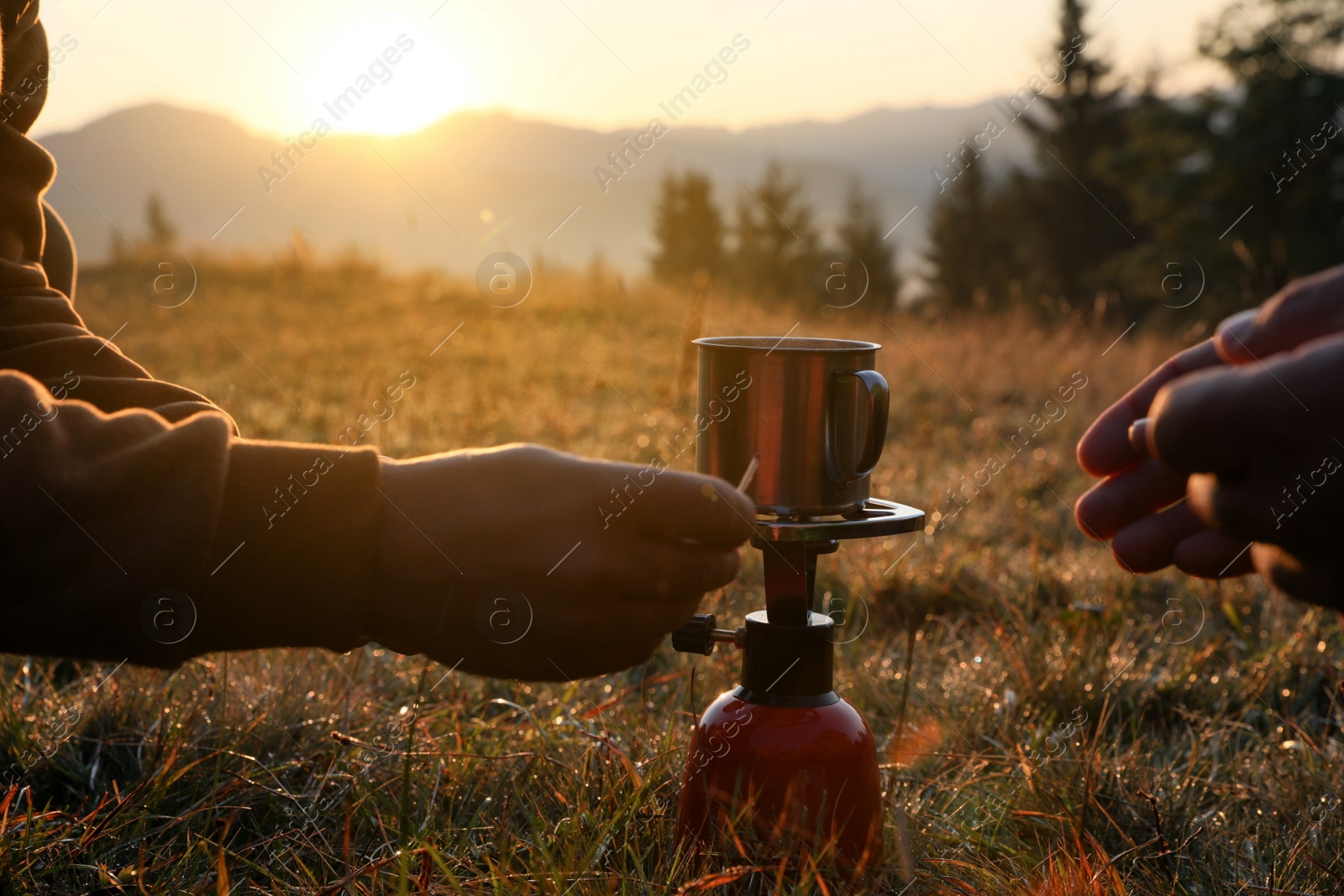 Photo of People making hot drink with portable gas burner in mountain camping, closeup