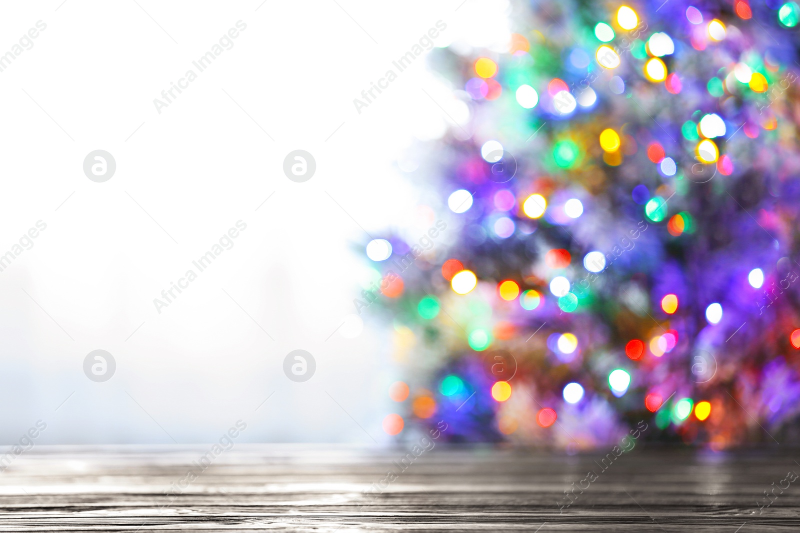 Photo of Blurred view of beautiful Christmas tree with colorful lights near window indoors, focus on wooden table. Space for text