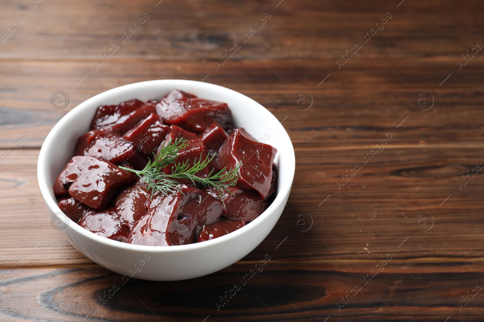 Photo of Cut raw beef liver with dill on wooden table, closeup. Space for text