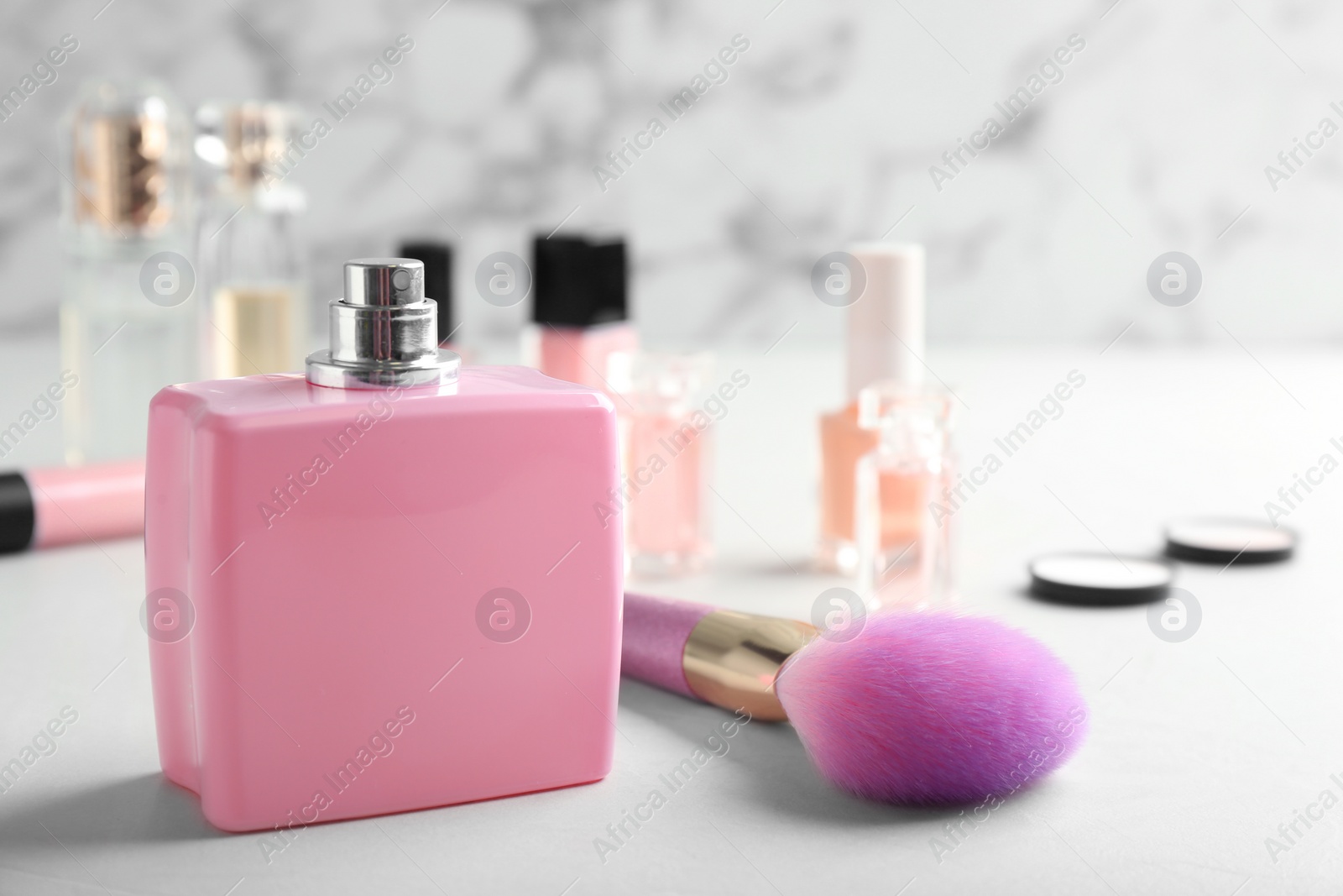 Photo of Bottle of perfume and cosmetic brush on table against marble background. Space for text