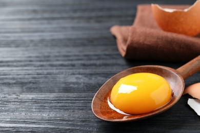 Spoon with raw egg yolk on black wooden table, closeup. Space for text