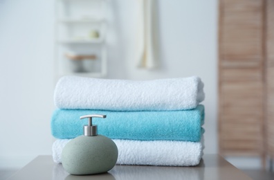 Clean towels and soap dispenser on table against blurred background