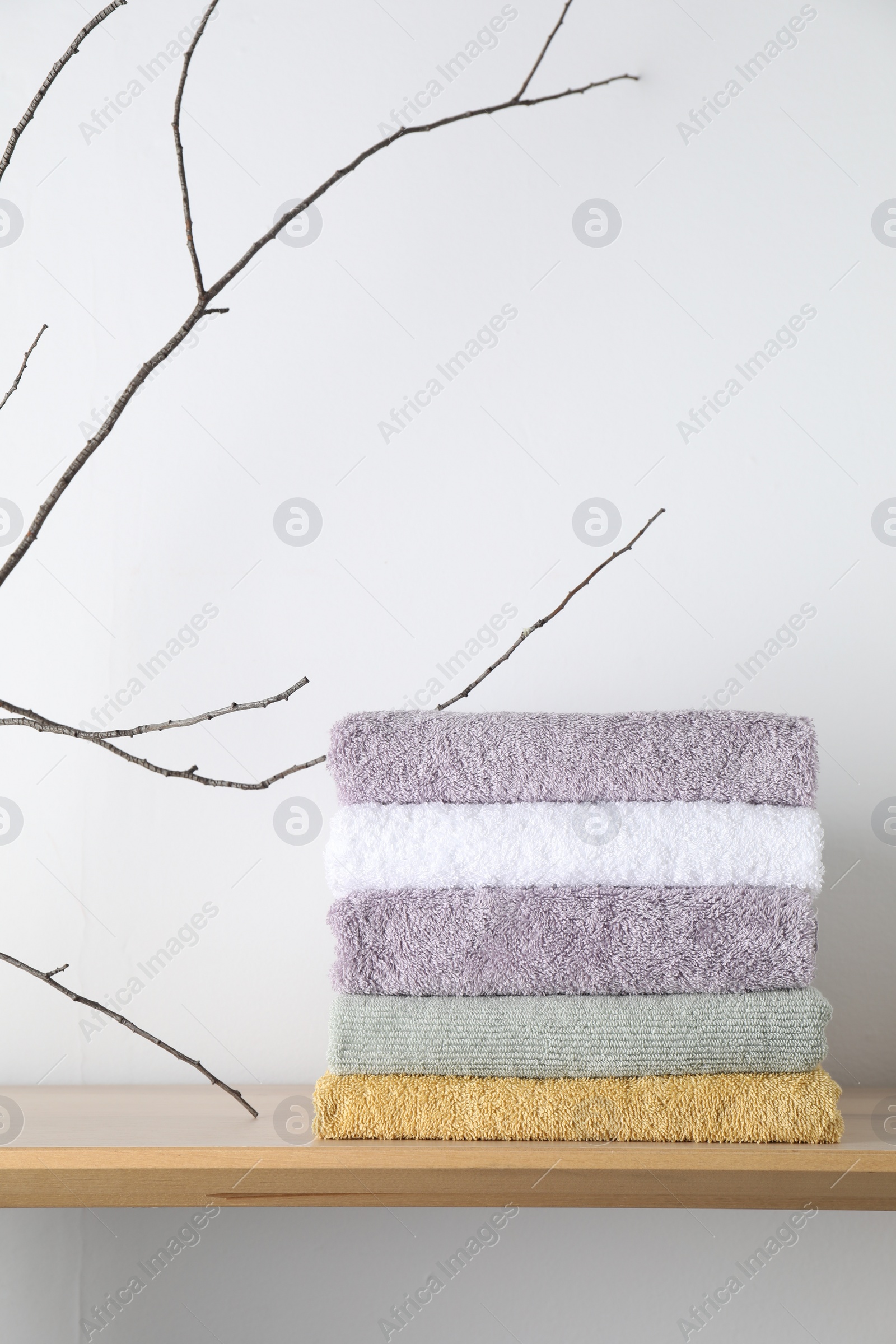 Photo of Stacked terry towels and tree branch on wooden shelf near white wall