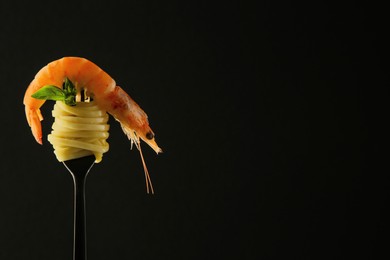 Photo of Fork with tasty pasta, shrimp and basil on black background, space for text