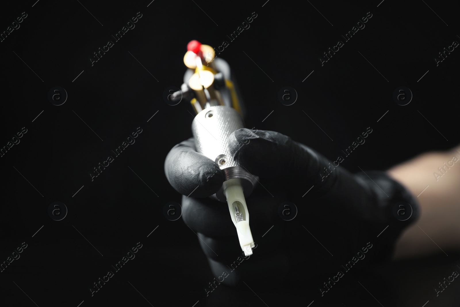 Photo of Tattoo artist with professional machine at table against black background, closeup